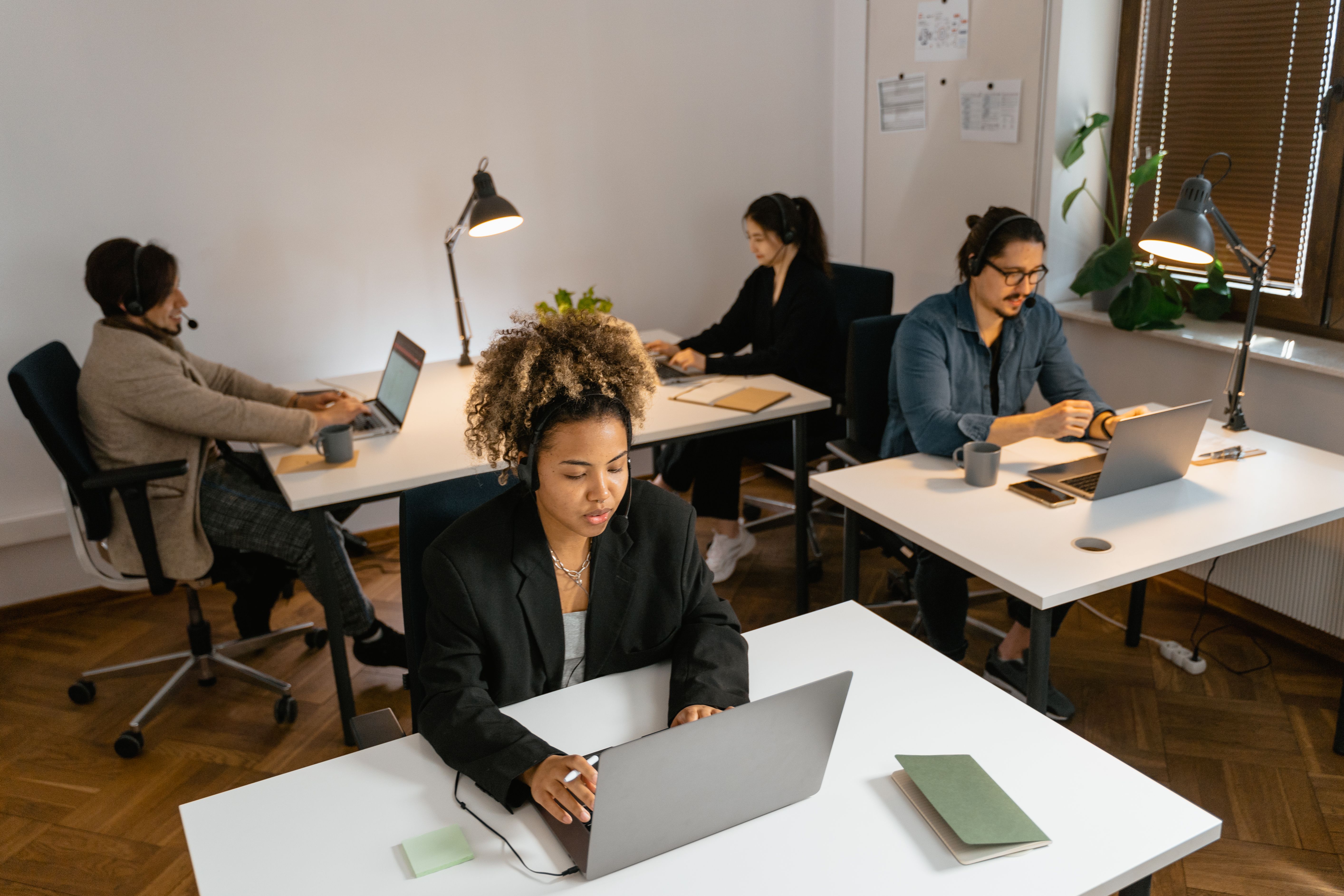 Operations coordinators working at laptops with headsets in an office